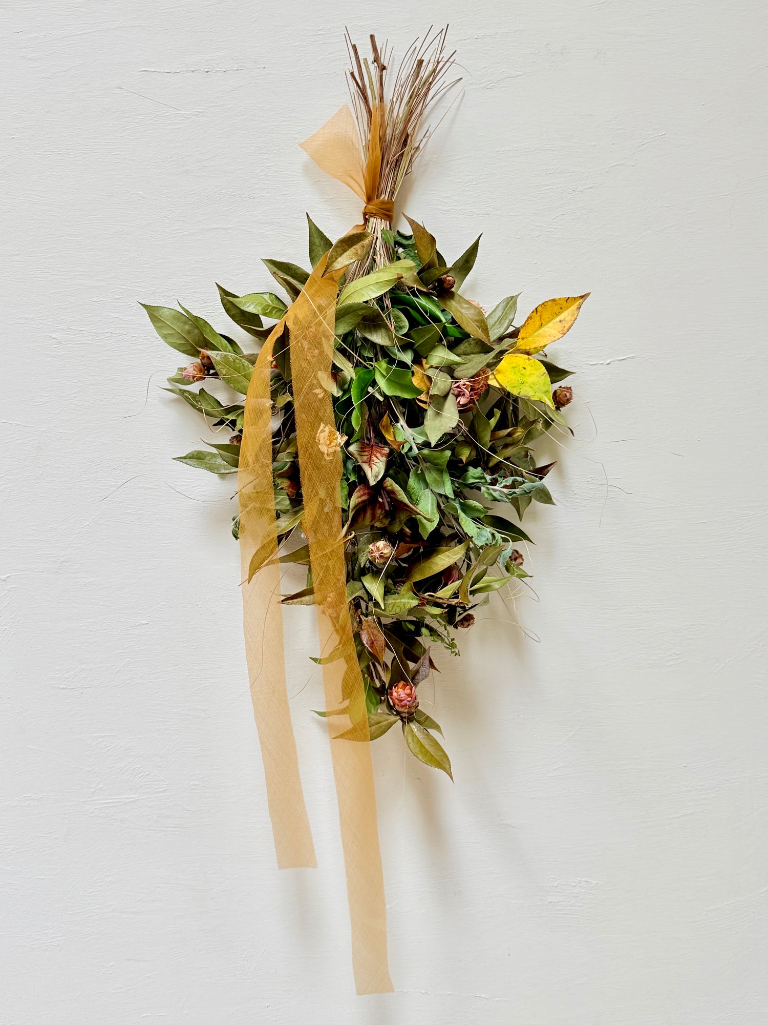 Handcrafted AWAKENING botanical swag with flowering Camellia, dried grasses, and natural foraged botanicals in warm earthy tones.