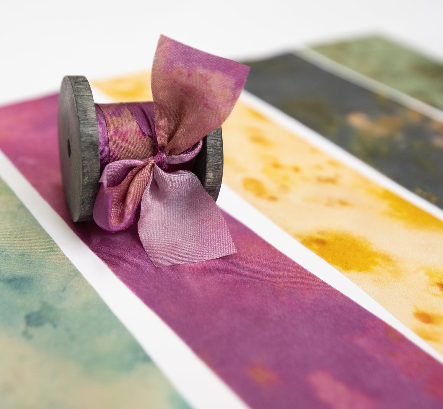 Botanical print silk ribbon in natural earthy tones displayed on FSC-certified wooden spools for wreath and floral styling.
