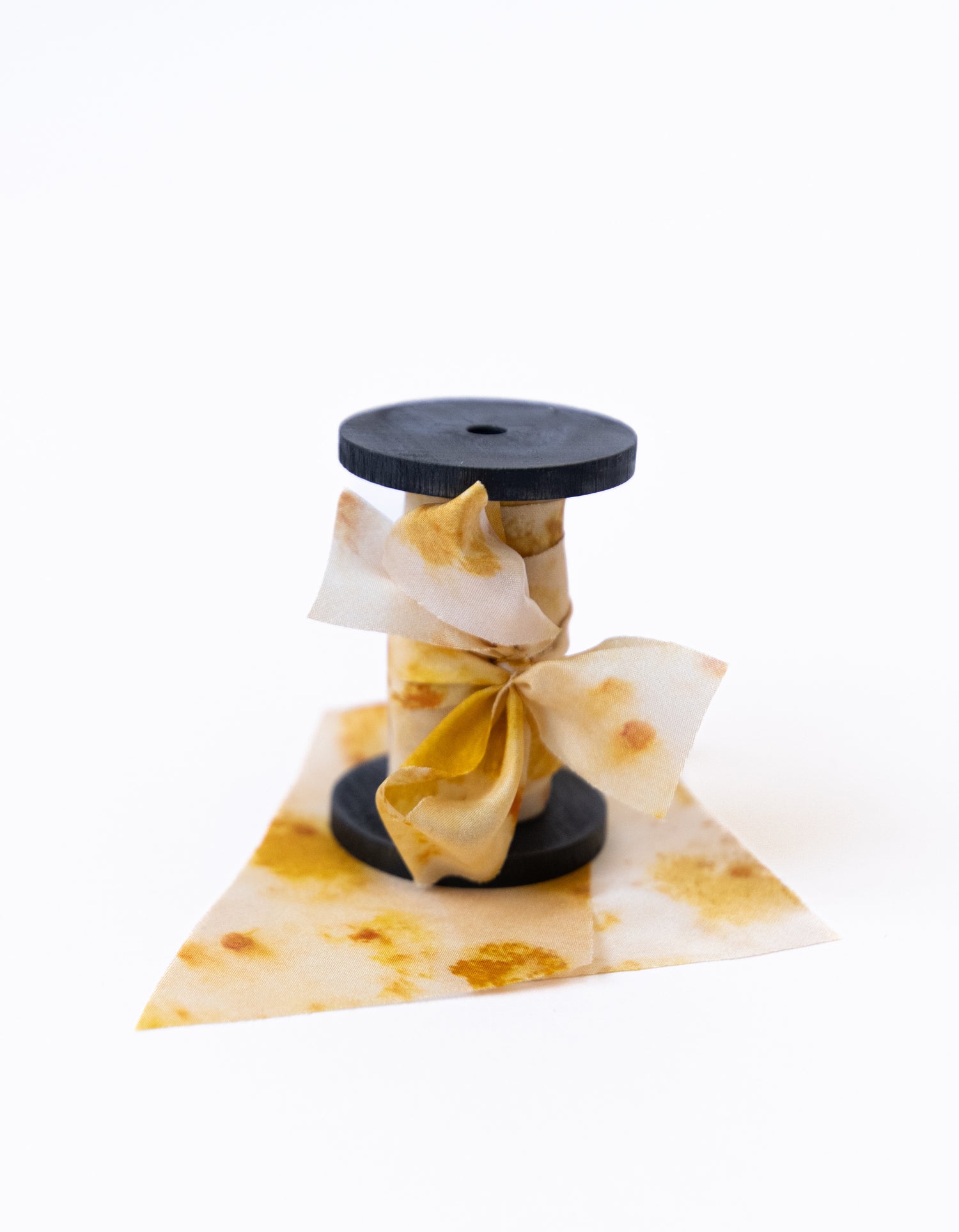 Botanical print silk ribbon in natural earthy tones displayed on FSC-certified wooden spools for wreath and floral styling.