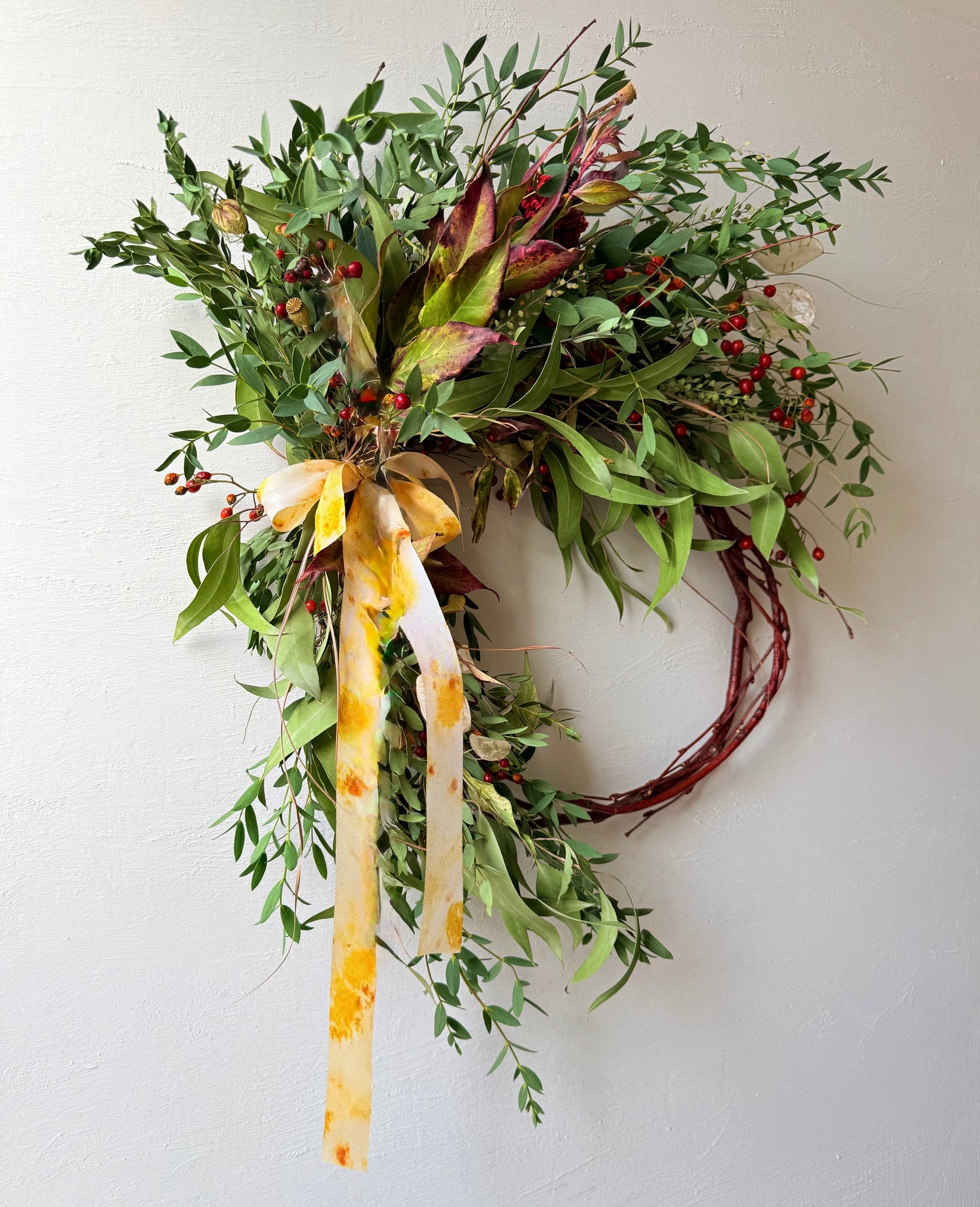 Handcrafted ANTICIPATION botanical wreath with dried dahlia, rose hips, eucalyptus, poppy seedheads, and natural grasses on a vine base in warm earthy tones.