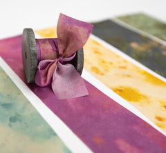 Botanical print silk ribbon in natural earthy tones displayed on FSC-certified wooden spools for wreath and floral styling.
