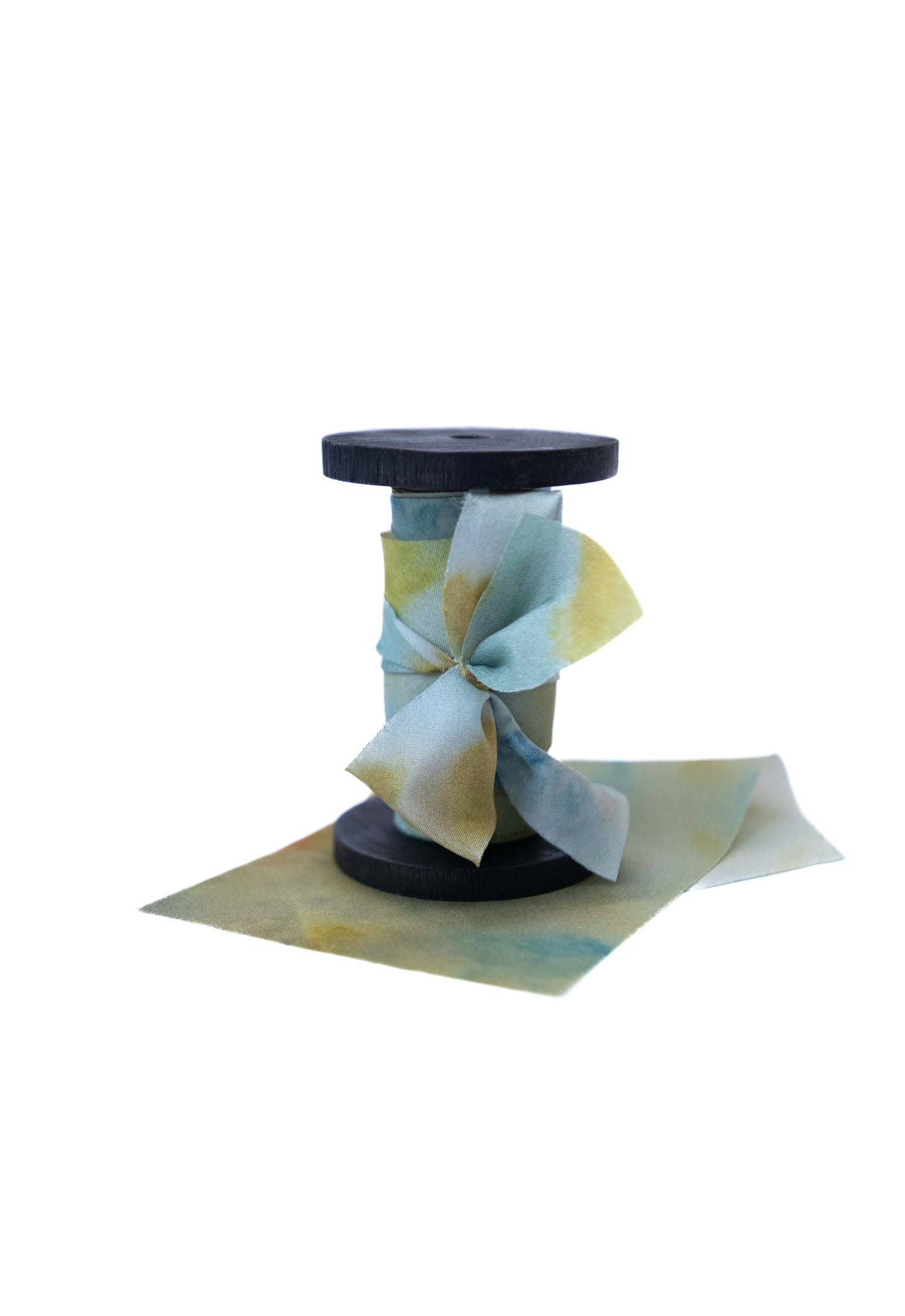 Botanical print silk ribbon in natural earthy tones displayed on FSC-certified wooden spools for wreath and floral styling.
